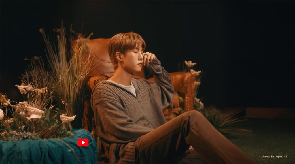 Lee Daeyeol sitting in a sunlit garden in the “Where Stars Grow” music video cover shoot, surrounded by greenery and soft golden star lighting, symbolizing his role as a steadfast tree and leader.