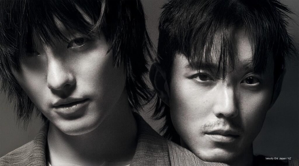 Woods and Justin H. Min pose in moody lighting, teasing their mystery short film “Slide Strum Mute” ahead of its February 26 release.