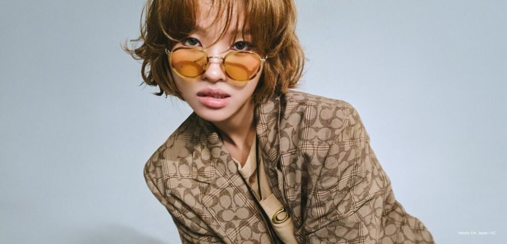 Soyeon of I-dle on the Marie Claire Taiwan April 2026 cover, wearing Coach Signature C blazer and wide-leg jeans, seated on folding chairs in a minimal grey room.