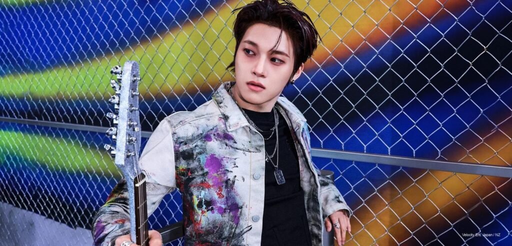 xikers member Junmin in a paint-splattered denim jacket holding a star guitar, leaning against a chain-link fence for ROUTE ZERO : The ORA concept photo.