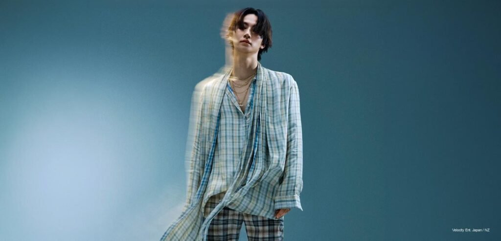 JAY B of GOT7 photographed for Numéro Netherlands June 2026 issue, wearing an oversized plaid shirt and layered gold chains against a cool blue-grey studio backdrop