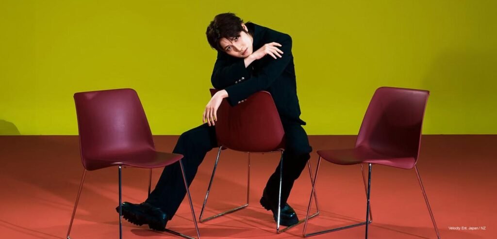 AEN “Always 1” Concept Photo — A New Era of Now Debut EP AEN member in an all-black tailored suit seated backward on a burgundy chair against a bold yellow and red backdrop, part of the "Always 1" concept photo series for debut EP "A New Era of Now."