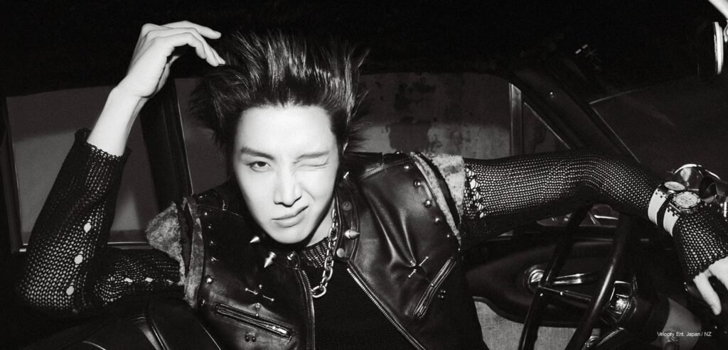 j-hope wearing a hooded top and Audemars Piguet watch, captured in a low-key motion pose against a dark, textured backdrop.