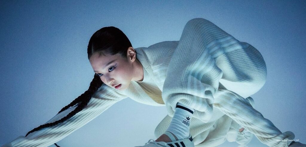 JENNIE Adidas Originals Campaign | Kpoppie Mag JENNIE in a white Adidas Originals outfit captured in a dynamic airborne pose against a blue background.