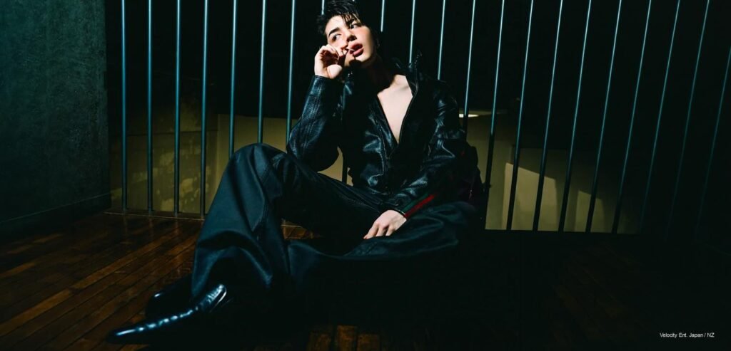 Maki x Gucci — Men’s Folio Singapore &TEAM's Maki seated on a wooden floor in a black Gucci leather jacket, backlit by vertical bar lighting, for Men's Folio Singapore's August 2026 cover.