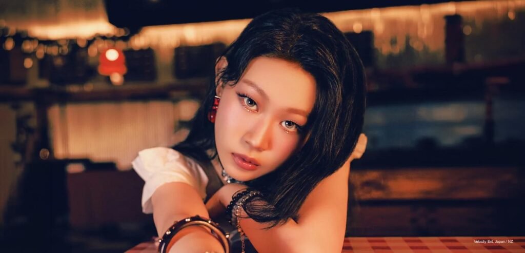 NINA — WHY NOT ME? Concept Photos NINA leans across a dim, amber-lit bar table, dark hair loose, one arm raised, red drop earring catching the light, for WHY NOT ME? concept photos.