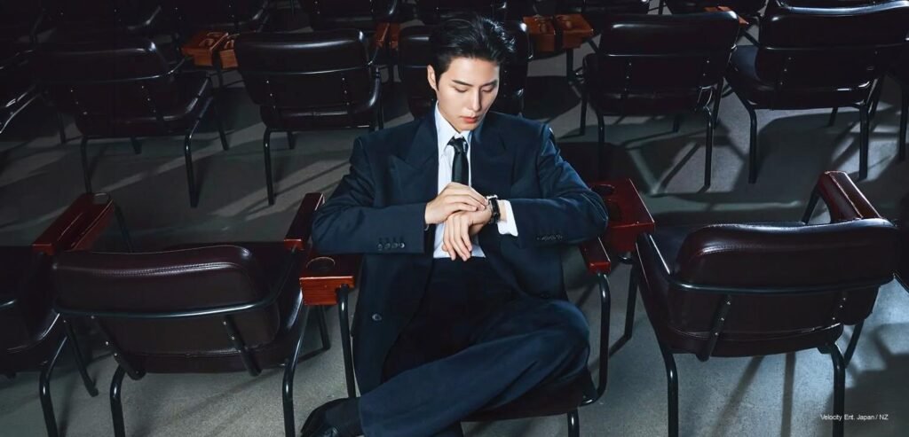 DAY6 Young K wearing a tailored dark suit checking his Hamilton wristwatch in a cinematic auditorium setting for Cosmopolitan Korea Men 2026 pictorial.