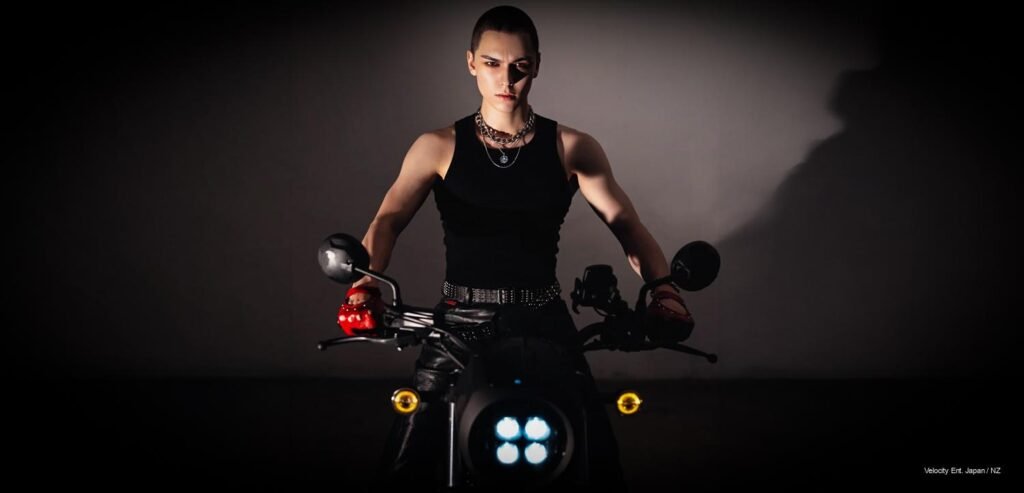 SEVENTEEN's Vernon sits powerfully on a black motorcycle wearing a black tank top and dark eye makeup in a dark NYLON France studio setting.