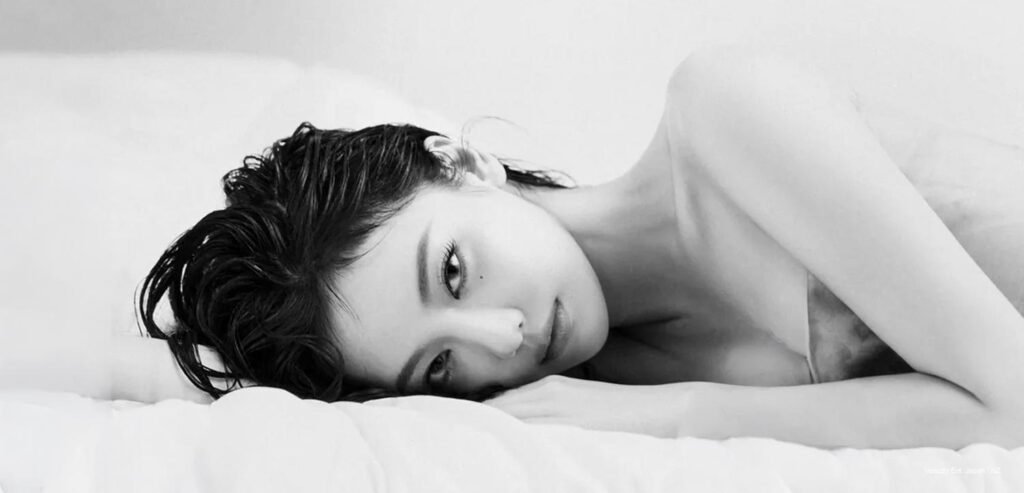 aespa's Ningning lying on white sheets in a striking monochrome visual for W Korea Beauty x Byredo editorial cover feature.