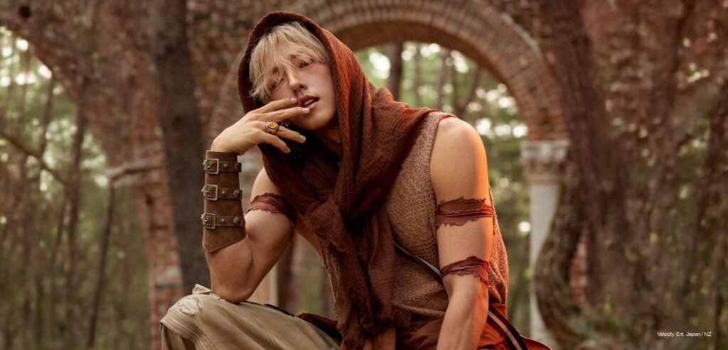 ALL'N wearing a hooded brown fabric wrap and leather bracer in a rustic archway for Four Seasons concept photo shoot.