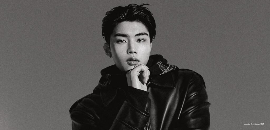 ZEROBASEONE Matthew & Gunwook x GQ Korea Black-and-white portrait of a ZEROBASEONE member in an oversized black leather jacket and plaid scarf, chin resting on his hand, for GQ Korea’s November 2026 pictorial